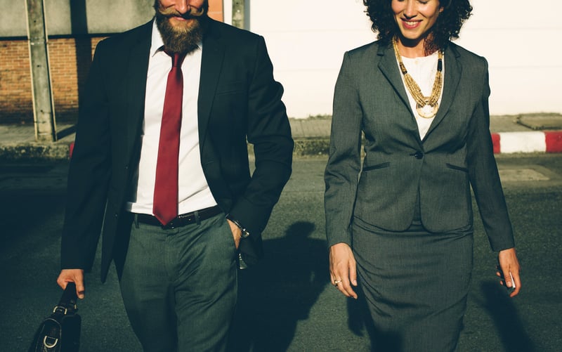 Bearded man in red tie and woman in business suit walking to work.